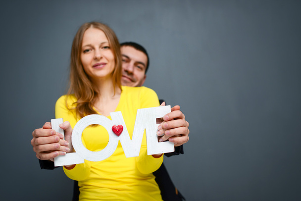 Beautiful smiling couple holding word LOVE , standing together on gray background - Foto, immagini
