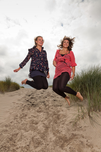 Two happy girls enjoying outdoor nature near the beach. Jumping in the air. Red and brown hair. Cloudy sky. - Photo, Image