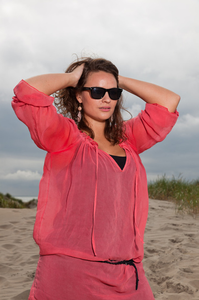 Happy young woman enjoying outdoor nature near the beach. Brown hair. Wearing pink shirt and black sunglasses. Cloudy sky. - Foto, Imagen