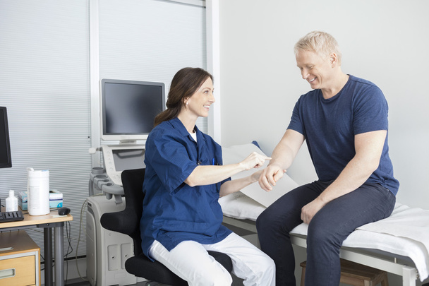 Hymyilevä lääkäri koskettaa miespotilaita käsin klinikalla
 - Valokuva, kuva