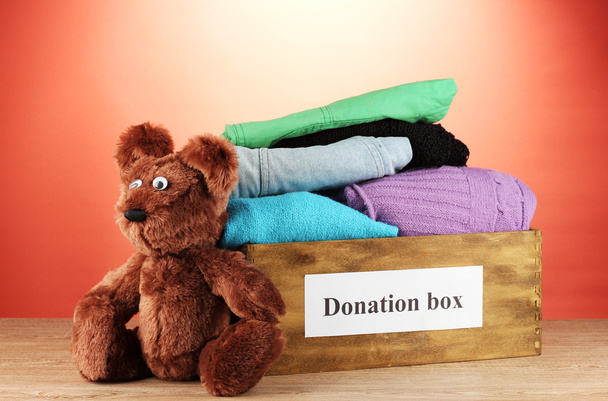 Donation box with clothing on red background close-up - Fotografie, Obrázek