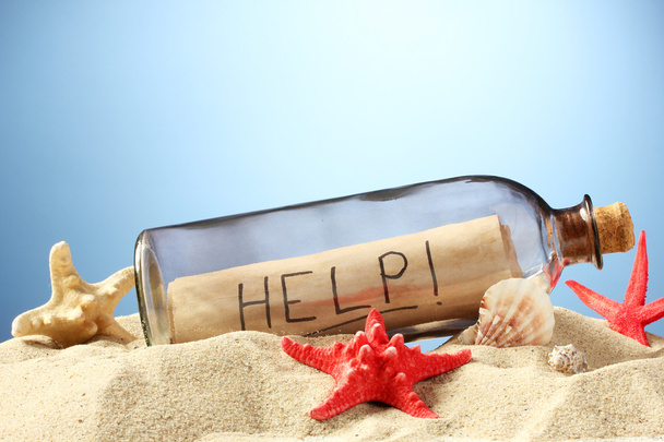 Glass bottle with note inside on sand, on blue background - 写真・画像