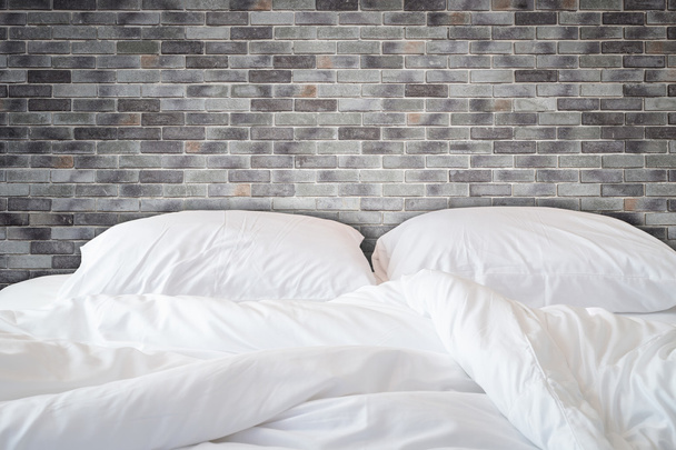 White bedding sheets and pillow on natural stone wall room backg - Foto, imagen