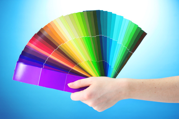 mão segurando paleta brilhante de cores no fundo azul
 - Foto, Imagem