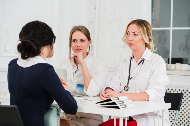 Dos mujeres muy jóvenes enfermeras o doctores hablando con una clienta en su oficina
 - Foto, Imagen
