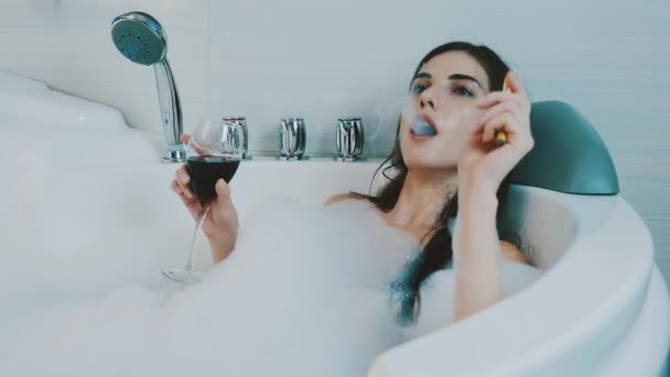 Chica relajarse en el baño lleno de espuma. Humo cigarrillo electrónico, vapor, vino tinto
. - Metraje, vídeo