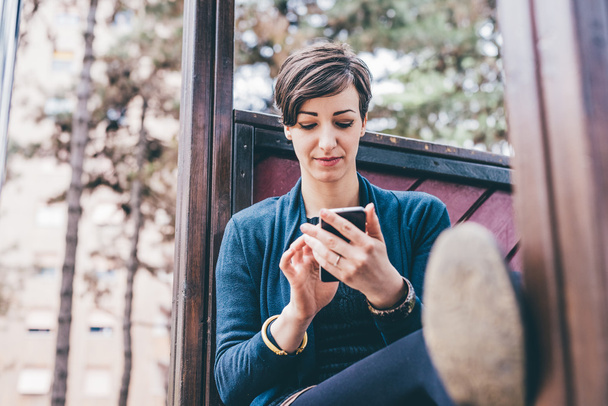 mujer sentada en un playgroung sosteniendo un teléfono inteligente
 - Foto, Imagen