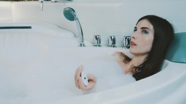 Chica joven tomar un baño lleno de espuma en el baño. Cambiar música por controlador
 - Metraje, vídeo