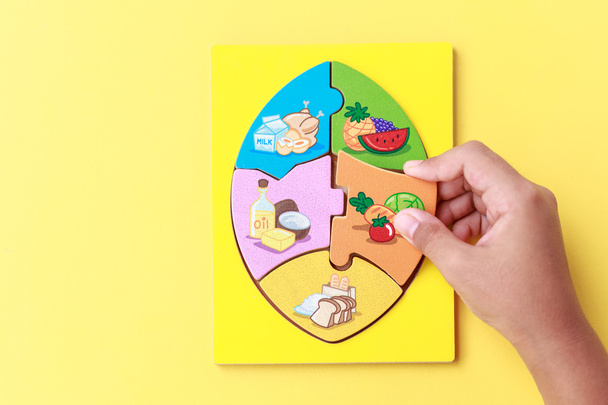 Hand of kid holding wooden jigsaw of the 5 food Groups. Child de - 写真・画像