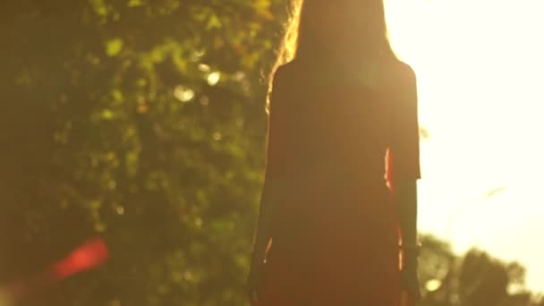 Hoikka tyttö siluetti kävelee aurinkoa vastaan puistossa. Hidastettu video, 120 fps
 - Materiaali, video