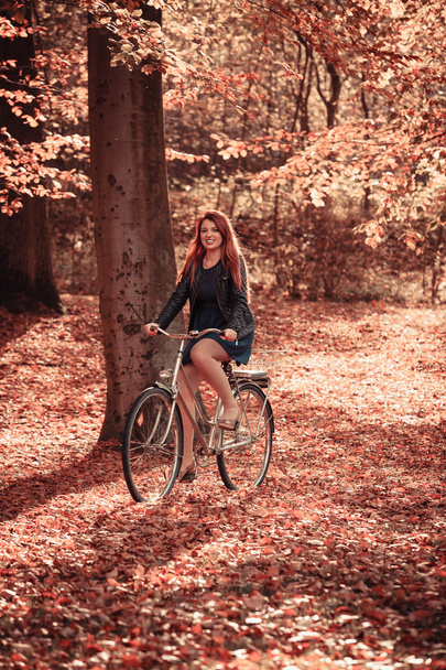 Redhead lady cycling in park. - Zdjęcie, obraz