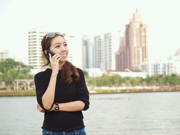 Pretty Asian calling by phone with building background - Photo, Image