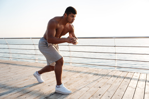 Young shirtless afro american sportsman doing squats on the pier - Foto, immagini