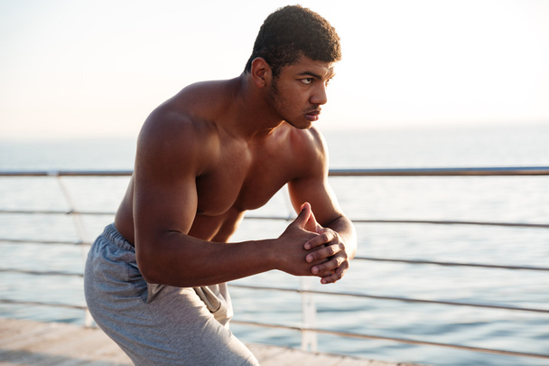 Young shirtless afro american sportsman doing squats on the pier - Foto, Imagem