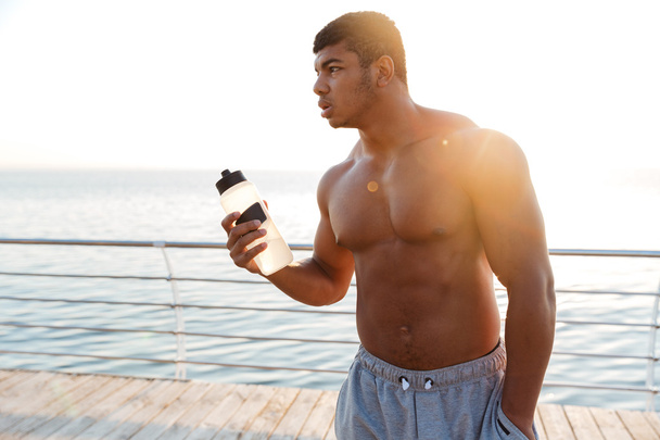 African man athlete standing on pier with bottle of water - Fotoğraf, Görsel