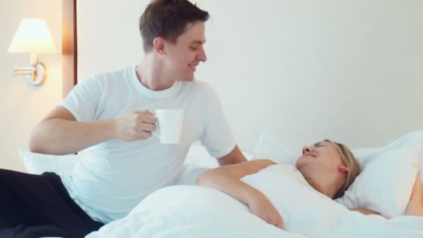 Man bring a cup of tea or coffee to woman sleeping in bed - Záběry, video