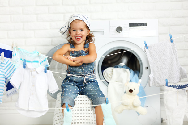 niño divertido feliz niña para lavar la ropa y se ríe en laund
 - Foto, Imagen
