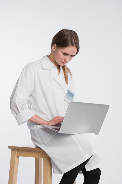 Smiling female doctor working on her laptop against a white background - Fotografie, Obrázek