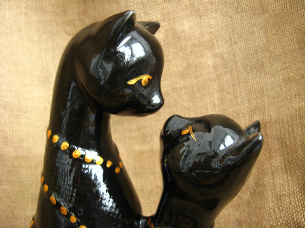 Дві іграшкові емальовані кішки на коричневому фоні
 - Фото, зображення