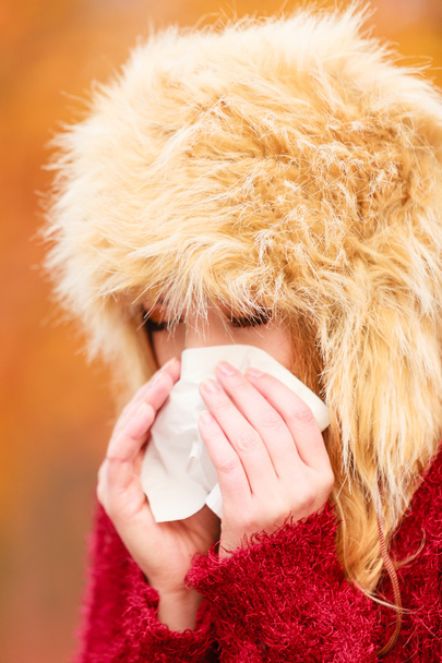 Sick woman in autumn park sneezing into tissue. - Фото, изображение