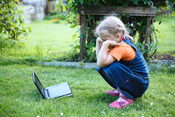 Little interested girl watching dvd movies on device in green lawn - Fotoğraf, Görsel