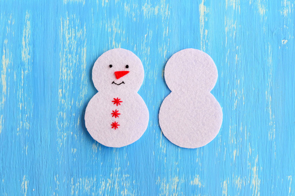 How to sew a Christmas snowman ornament. DIY Christmas decor handmade step by step. Cut from white felt details for sewing Christmas tree ornament. On one side embroidered with black thread eyes and mouth, red thread snowflakes and nose  - Photo, Image