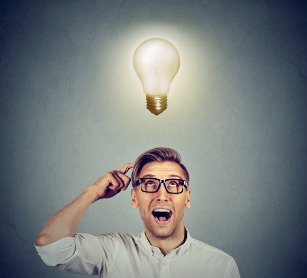 Happy man in glasses looking up at bright light idea bulb above head  - Foto, imagen
