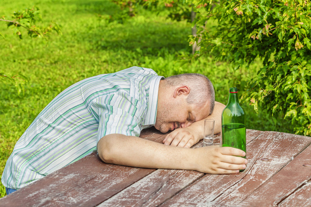Μεθυσμένος άντρας που κοιμάται κοντά σε μπουκάλι οινόπνευμα στον πίνακα  - Φωτογραφία, εικόνα