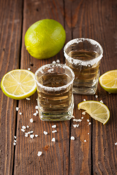 Makrofokus-Foto von Aufnahmen goldener mexikanischer Tequila mit Limette und Salz auf Holzgrund. Konzept für alkoholische Getränke. - Foto, Bild
