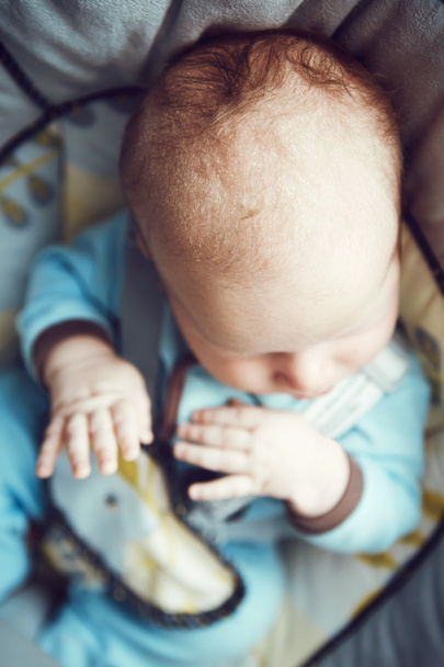 Retrato de lindo adorable blanco caucásico durmiendo pequeño bebé recién nacido en ropa azul sentado en silla oscilante, vista de su cabeza manos desde arriba, posición embrión feto
 - Foto, Imagen