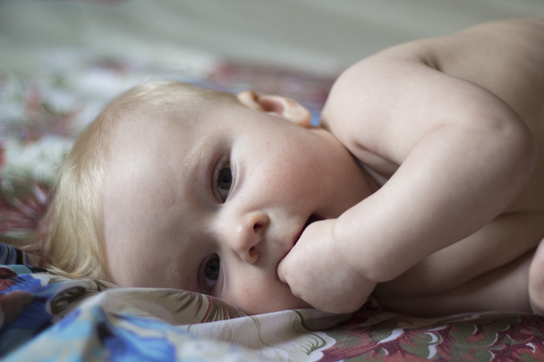 Cute baby lying on the bed with fingers in his mouth, soft focus - Photo, Image