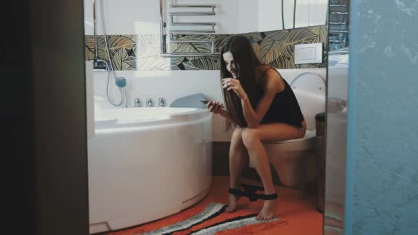 Young girl sit on toilet. Tap on smartphone. Smoke electronic cigarette. Steam - Filmati, video
