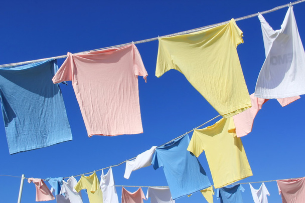 T-shirts penduradas na corda na frente do céu azul
 - Foto, Imagem
