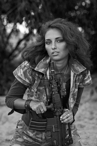 Οπλισμένοι όμορφη νεαρή γυναίκα στο καμουφλάζ με τουφέκι στην παραλία. - Φωτογραφία, εικόνα