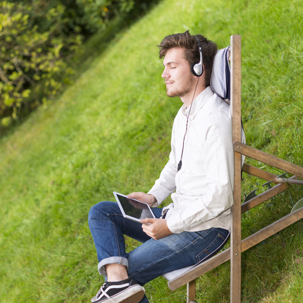 Nahaufnahme eines Studenten, der im Freien mit geschlossenen Augen Musik hört - Foto, Bild