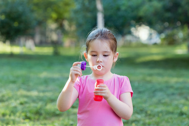 A little girl blowing soap bubbles in a park - Photo, Image