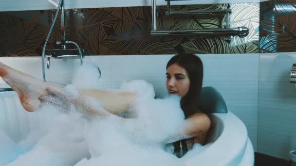 Chica feliz tomar un baño lleno de espuma en el baño. Bañera. Soplar espuma de jabón. Lavado
 - Imágenes, Vídeo