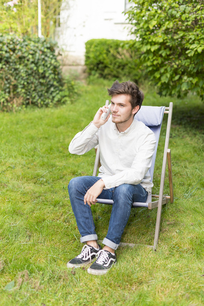 Bahçede oturan telefonda sevimli sarışın genç - Fotoğraf, Görsel