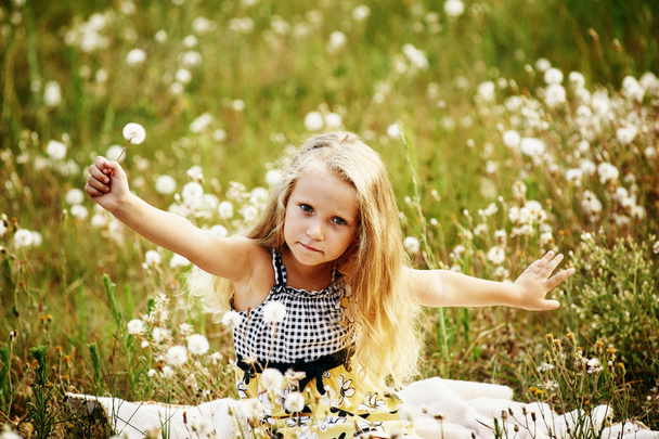小さな女の子はタンポポと草原で遊んでいる - 写真・画像