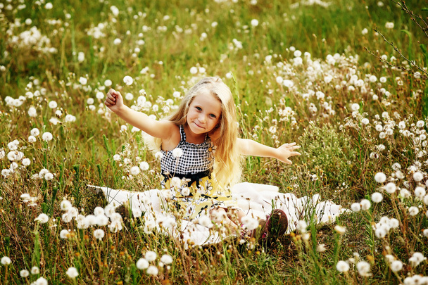 klein meisje spelen in de weide met paardebloemen - Foto, afbeelding