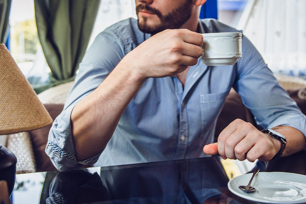 Brodaty mężczyzna siedząc z filiżanką kawy rano i patrząc przez okno - Zdjęcie, obraz