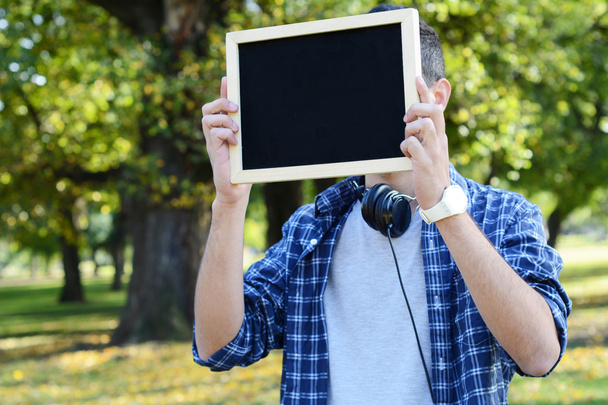 Young man with black headphones holding chalkboard . - Foto, immagini