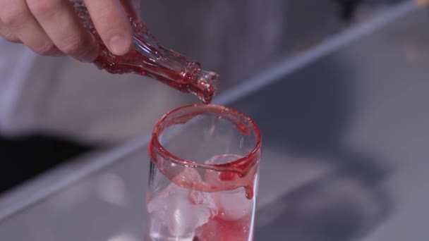 Adding red syrup to the glass with ice - Filmati, video