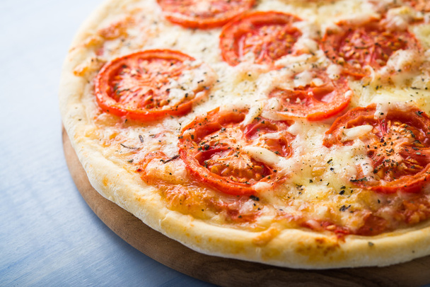 Pizza mit Tomate, Käse und trockenem Basilikum auf blauem Holzgrund in Großaufnahme. Italienische Küche. - Foto, Bild