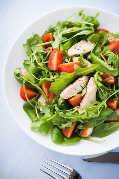 Ensalada fresca con pollo, tomate y verduras (espinacas, rúcula) sobre fondo de madera azul vista superior. Alimento saludable
. - Foto, imagen