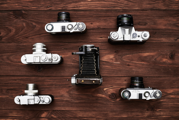 Коллекция старинных фотоаппаратов, хорошо расставленных по деревянной спинке
 - Фото, изображение