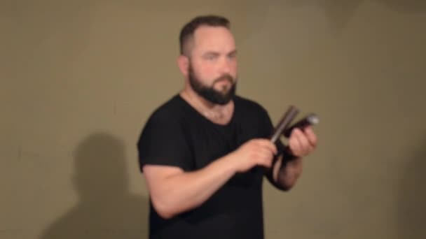 Ein Mann mit Bart und schwarzem T-Shirt spielt auf dem Schlaginstrument Claves. auf dem hellen Wandhintergrund. - Filmmaterial, Video