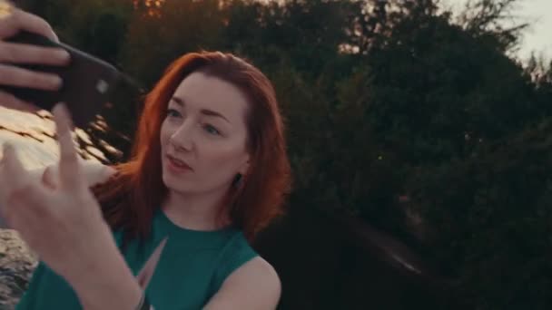 Happy red hair girl in turquoise dress take selfie on sailing motor boat. Sunset - Footage, Video