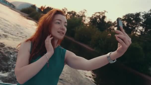 Young red hair girl in turquoise dress take selfie on sailing motor boat. Sunset - Footage, Video