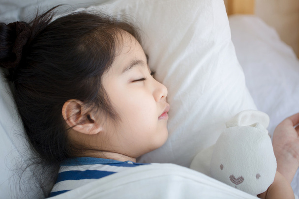Pequeña chica asiática abrazando a la muñeca y durmiendo en la cama
 - Foto, imagen